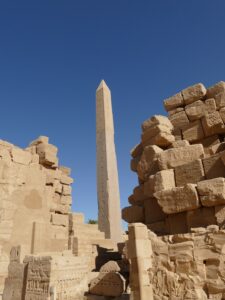 Tall granite obelisk with hieroglyphs at Karnak Temple in Luxor, Egypt surrounded by sandstone ruins