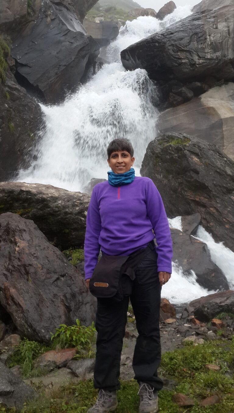 Poorti standing in front of a small cascading waterfall on the Hampta Pass trail