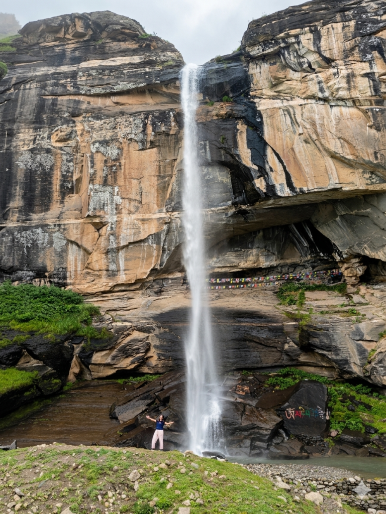 Tall waterfall flowing down rocky cliff into a small pool with a person standing below in Pangi Valley.