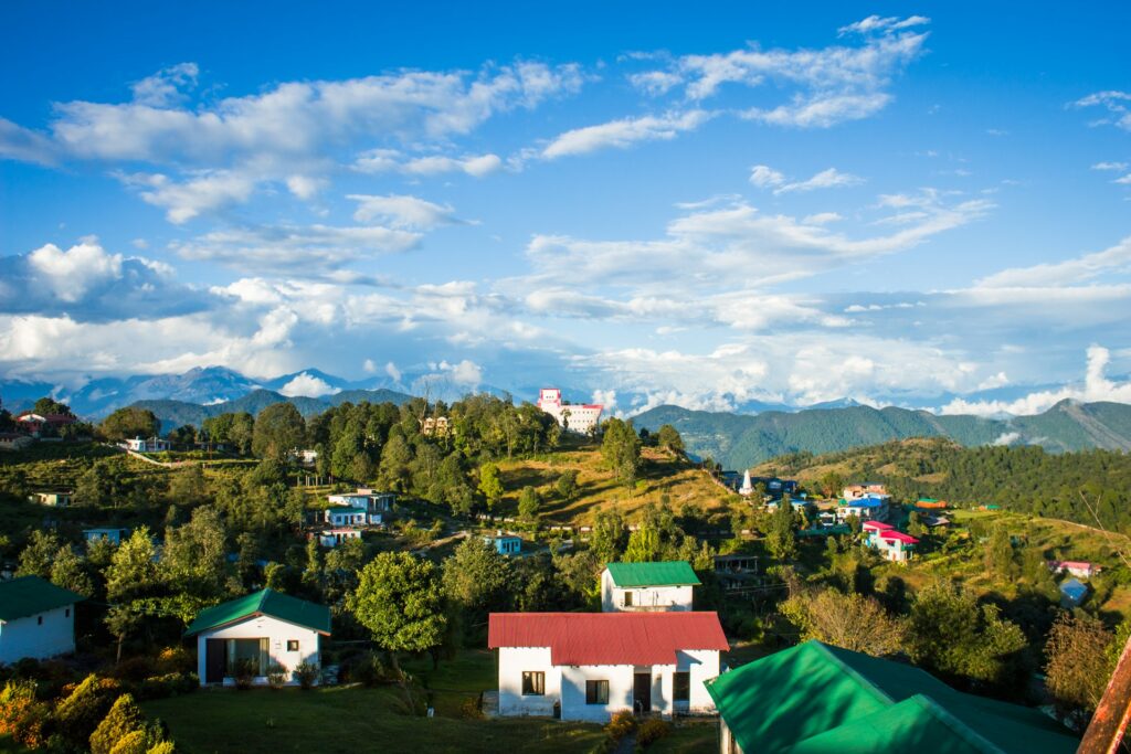 A scenic view of a mountain village with white houses and colorful roofs under a blue sky with scattered clouds.
