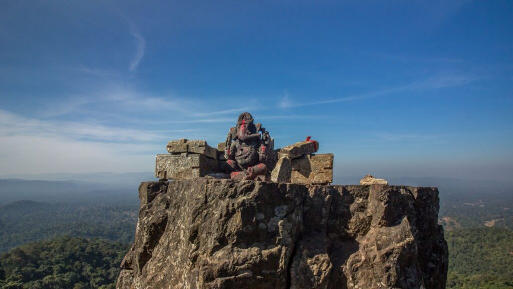 An ancient 1,000-year-old stone idol of Lord Ganesha perched on a rocky mountain peak overlooking the lush Bailadila valley forests in Chhattisgarh.