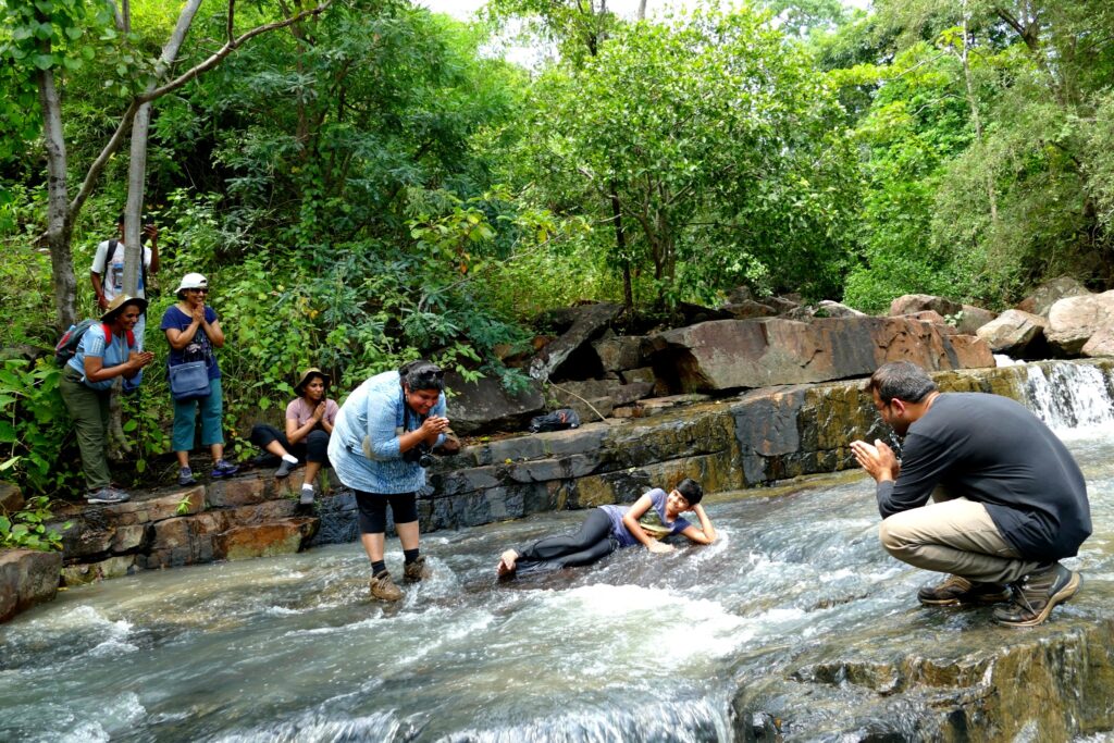 Travellers enjoying a shallow forest stream near a waterfall in Bastar.