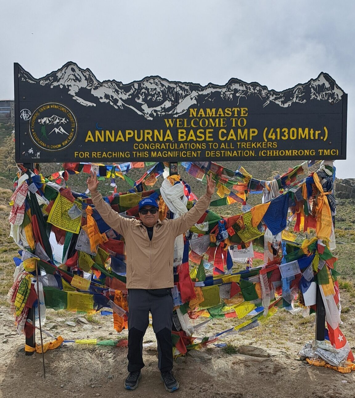posing beneath the Annapurna Base Camp (4,130 m) signboard in Nepal after completing the Annapurna Base Camp Trek.
