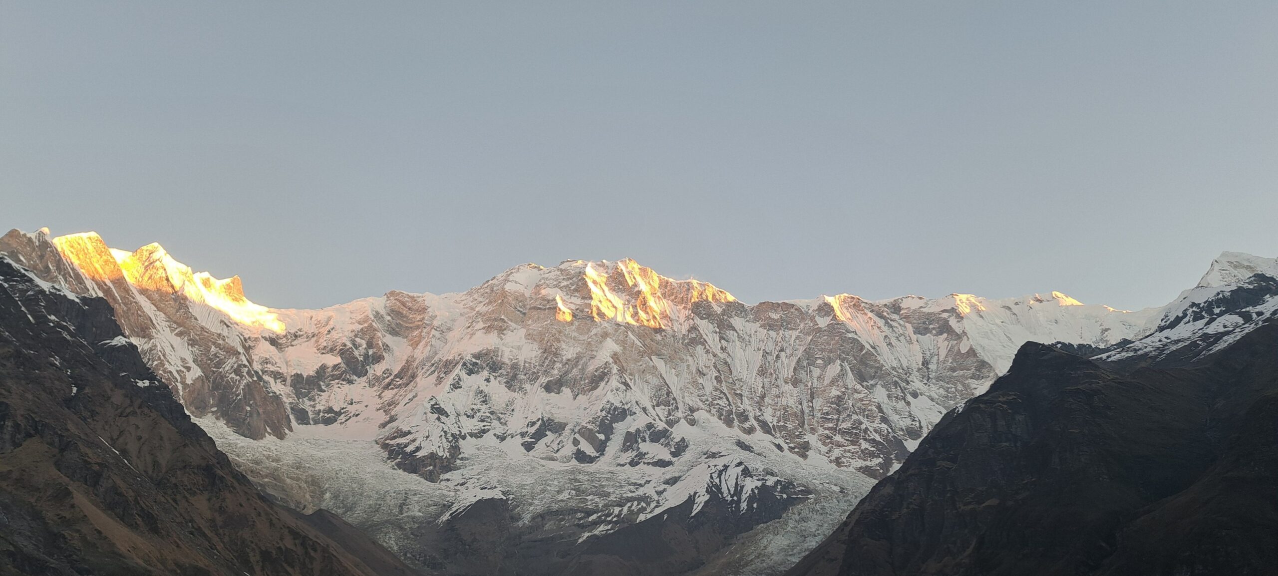 Sunrise over the Annapurna Amphitheatre from Annapurna Base Camp, with Annapurna I and surrounding snow-covered Himalayan peaks glowing in golden light.
