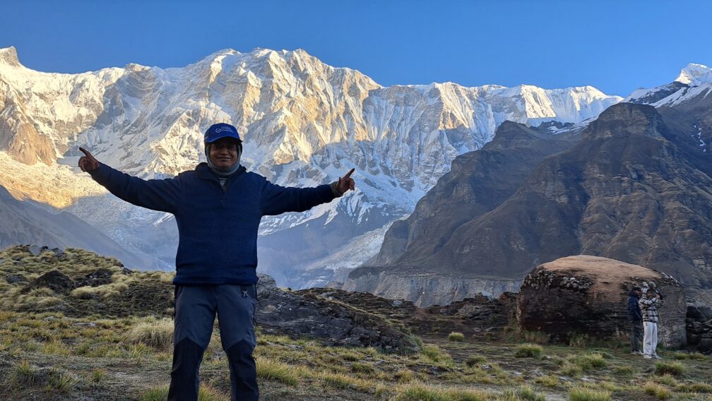 Trekker posing at Annapurna Base Camp with the snow-covered Annapurna massif and Himalayan mountains in Nepal.