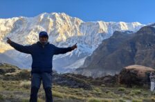 Trekker posing at Annapurna Base Camp with the snow-covered Annapurna massif and Himalayan mountains in Nepal.