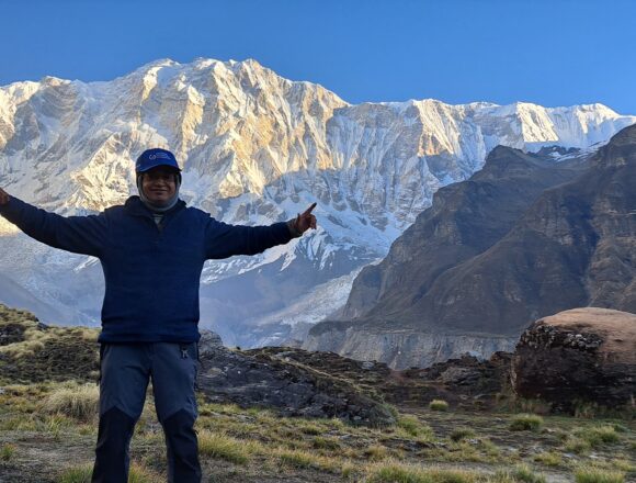 Trekker posing at Annapurna Base Camp with the snow-covered Annapurna massif and Himalayan mountains in Nepal.