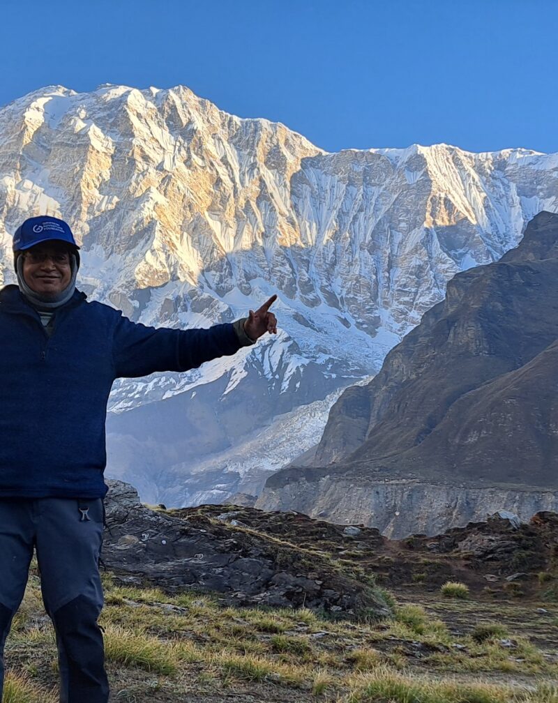 Trekker posing at Annapurna Base Camp with the snow-covered Annapurna massif and Himalayan mountains in Nepal.