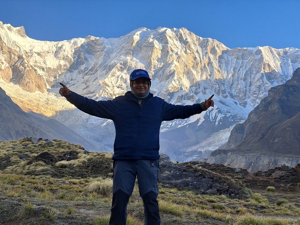 Trekker posing at Annapurna Base Camp with the snow-covered Annapurna massif and Himalayan mountains in Nepal.